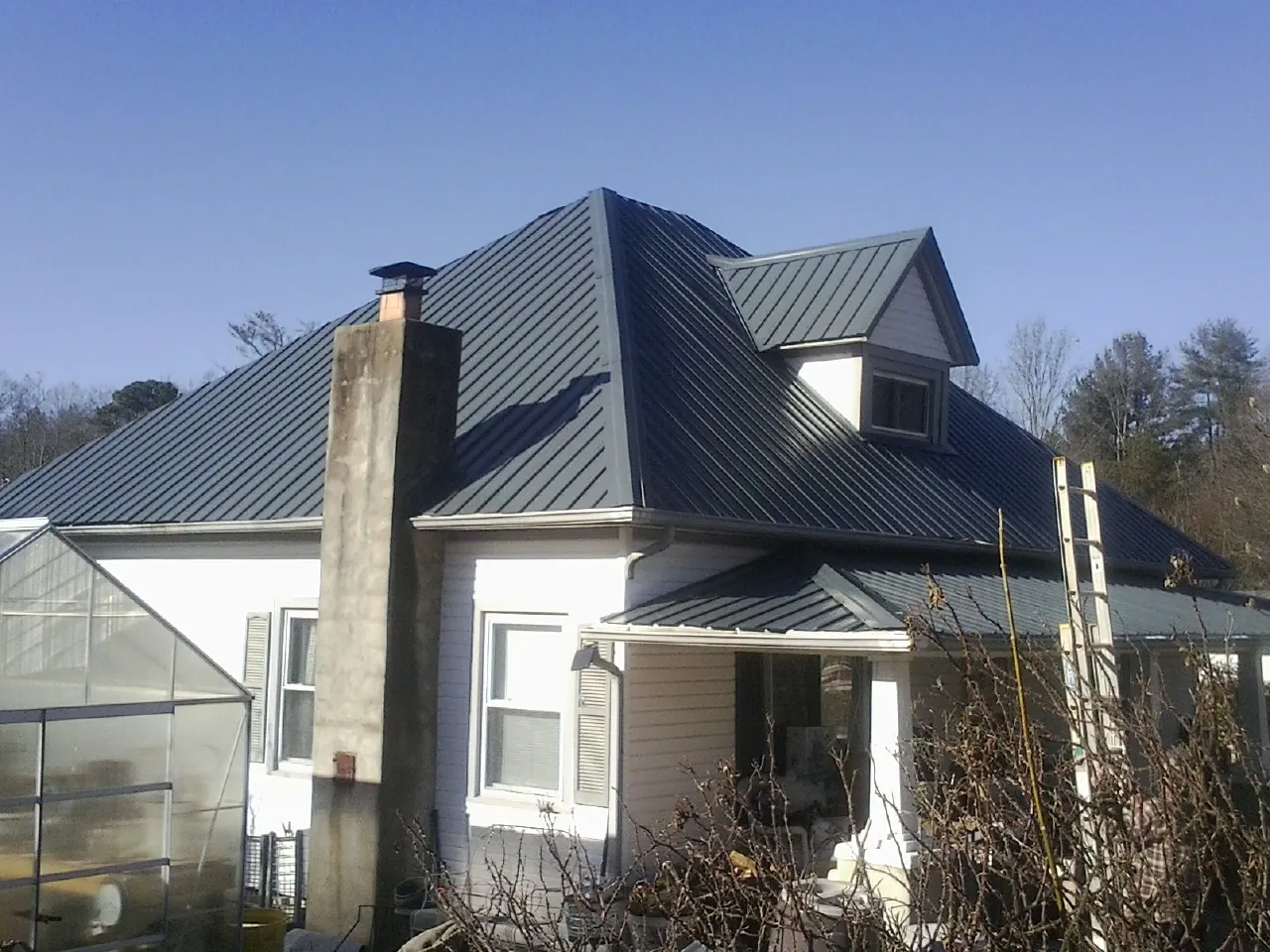 Dark blue standing seam metal roof on a white farmhouse with dormer — Slate & Tile Roof Repair by Roofing Brothers in Island Park