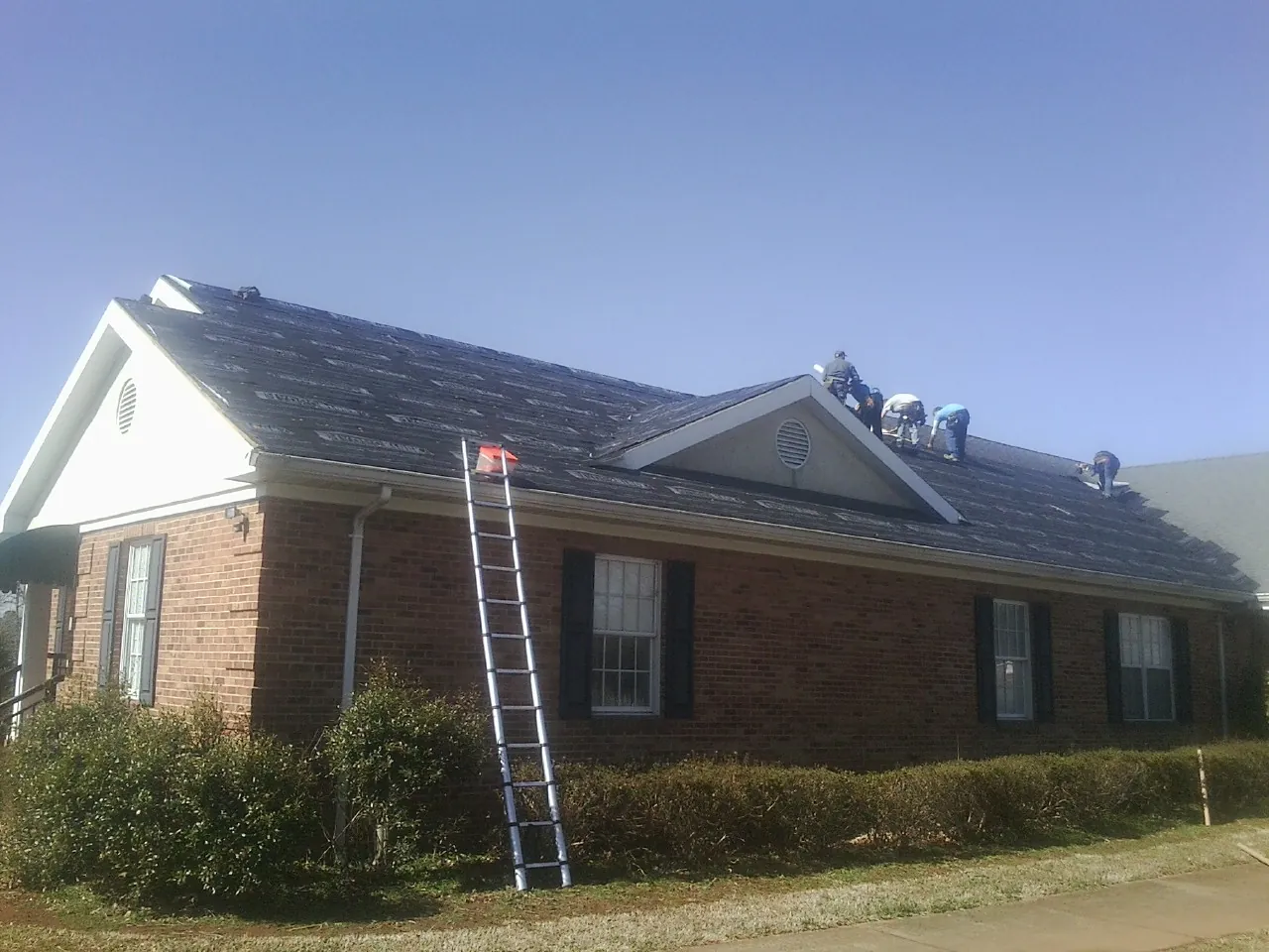 Crew tearing shingles off a brick ranch roof with a ladder set — Emergency Roof Repair work by our crew in Island Park