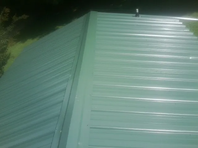 New green metal panels meeting at the ridge of a roof — Flat Roof Repair work by our crew in Island Park
