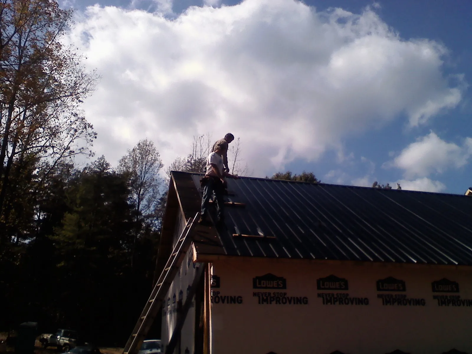 Roofer fastening dark metal panels high against a cloudy sky, from a Roof Inspection job in Island Park