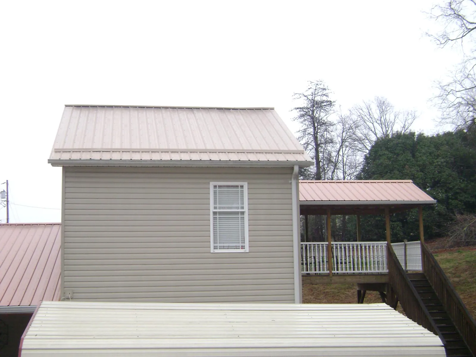 Tan metal roofs on a two story addition and attached porch, from a Roof Replacement job in Island Park